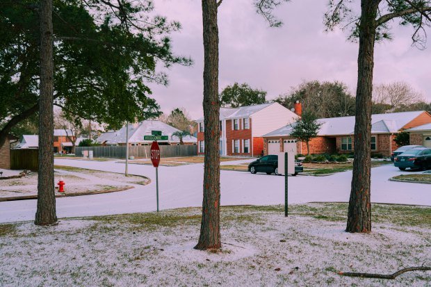A serene suburban street covered in snow, featuring houses and trees on a winter day.
